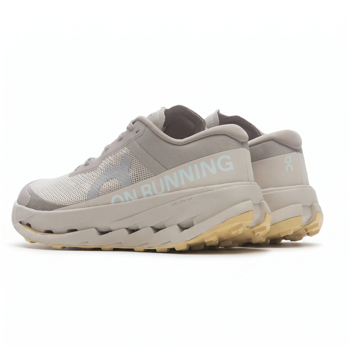 A pair of On Running running shoes in light gray and beige, featuring a chunky midsole, mesh upper, and light blue 'ON RUNNING' text on the side, set against a plain white background.