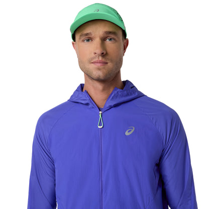 Man wearing a blue running jacket and black shorts with a green cap on a white background