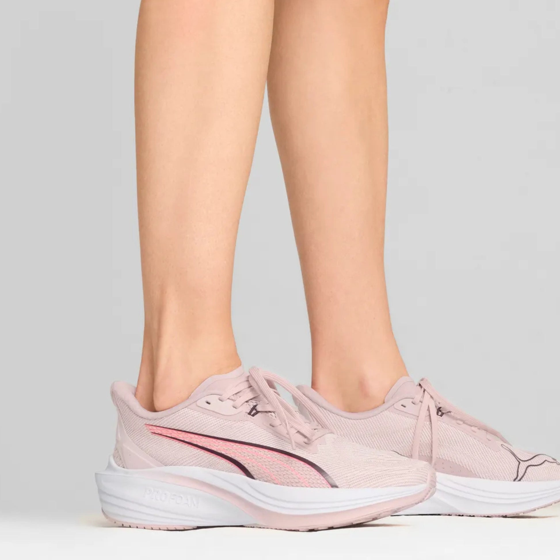 Pink Puma running shoes worn by a person on a light gray background