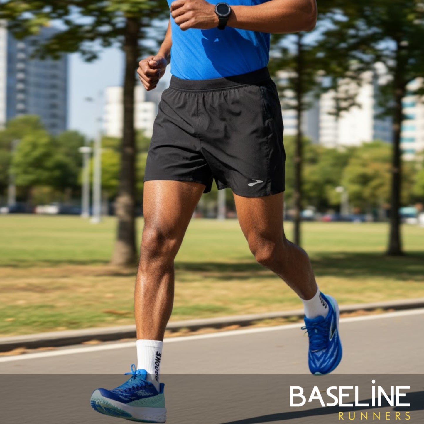 Person running on a path with trees and buildings in the background, wearing blue shoes and black running shorts.