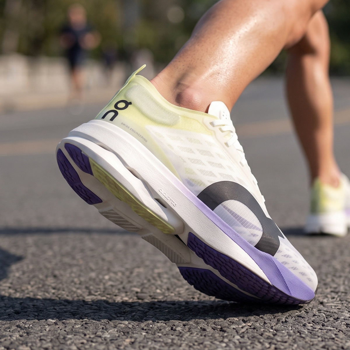 A close-up of a running shoe being worn, captured mid-step on an asphalt road. The shoe is white with a pale yellow-green upper, a black logo, and purple accents on the midsole and outsole.