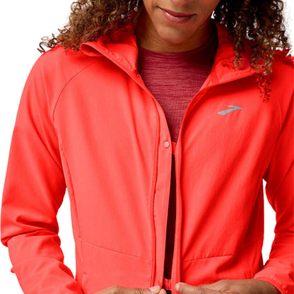 Woman wearing a orange jacket with a Brooks logo on a white background