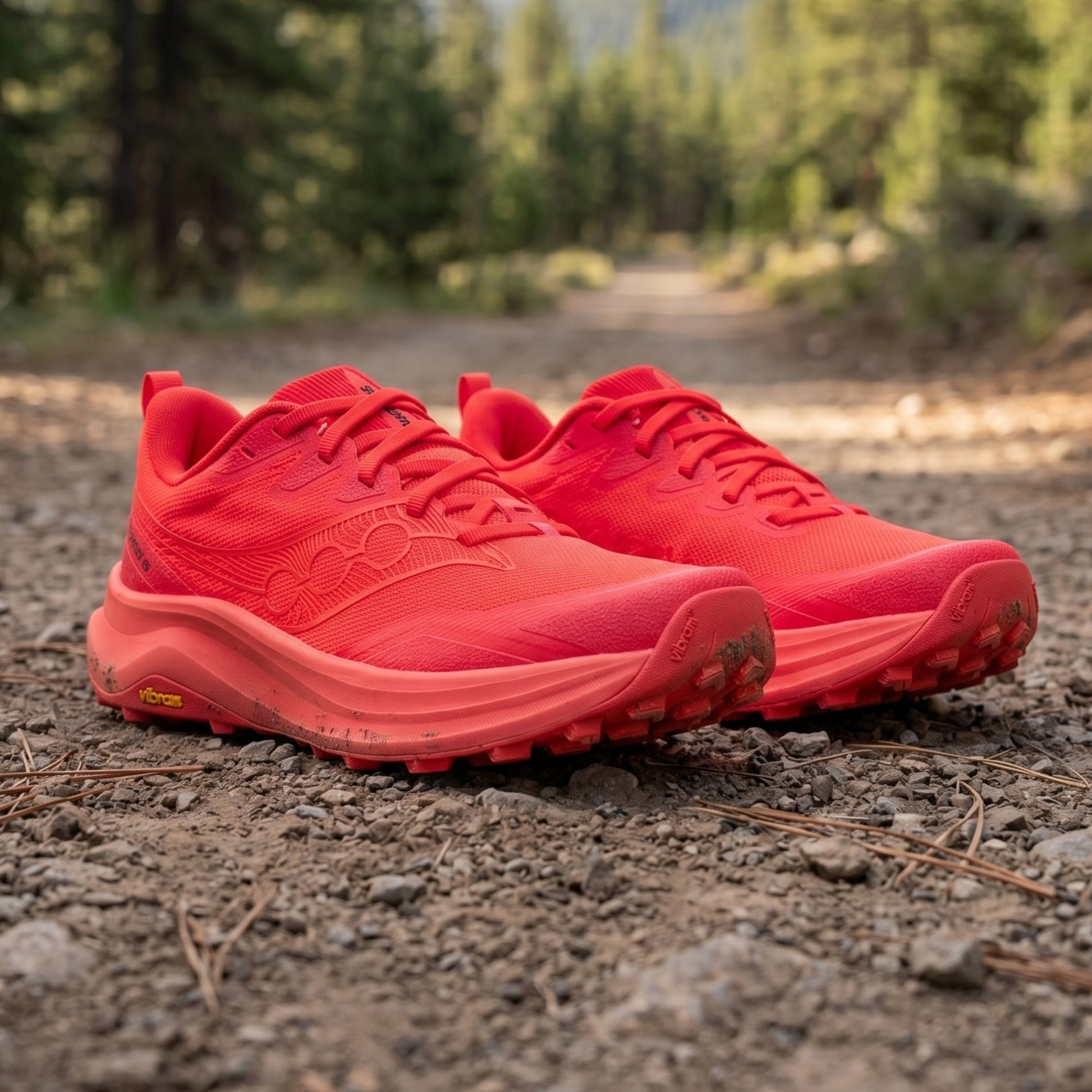 Red Saucony running shoes on a dirt path with greenery in the background