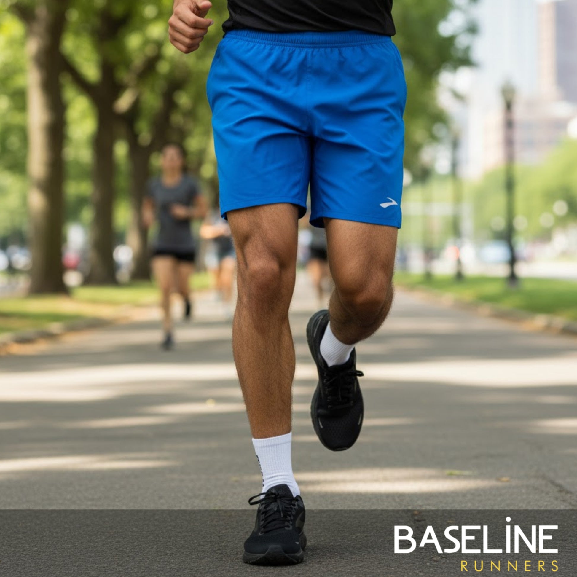 Person running on a street wearing blue running shorts and black shoes, with 'Baseline Runners' branding.
