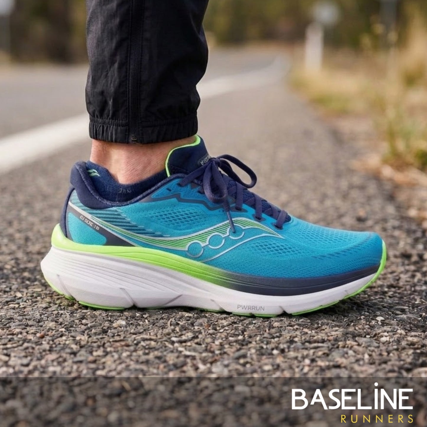 Person wearing a blue and green Saucony running shoe on a road with 'Baseline Runners' branding
