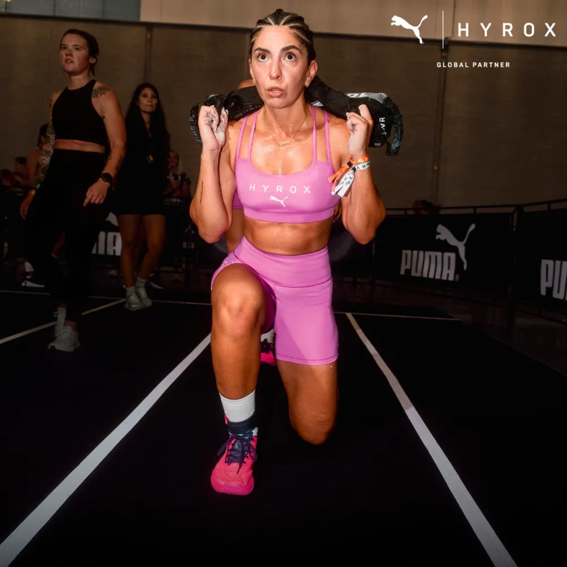 Woman exercising with weights at a HYROX fitness event, surrounded by Puma branding.