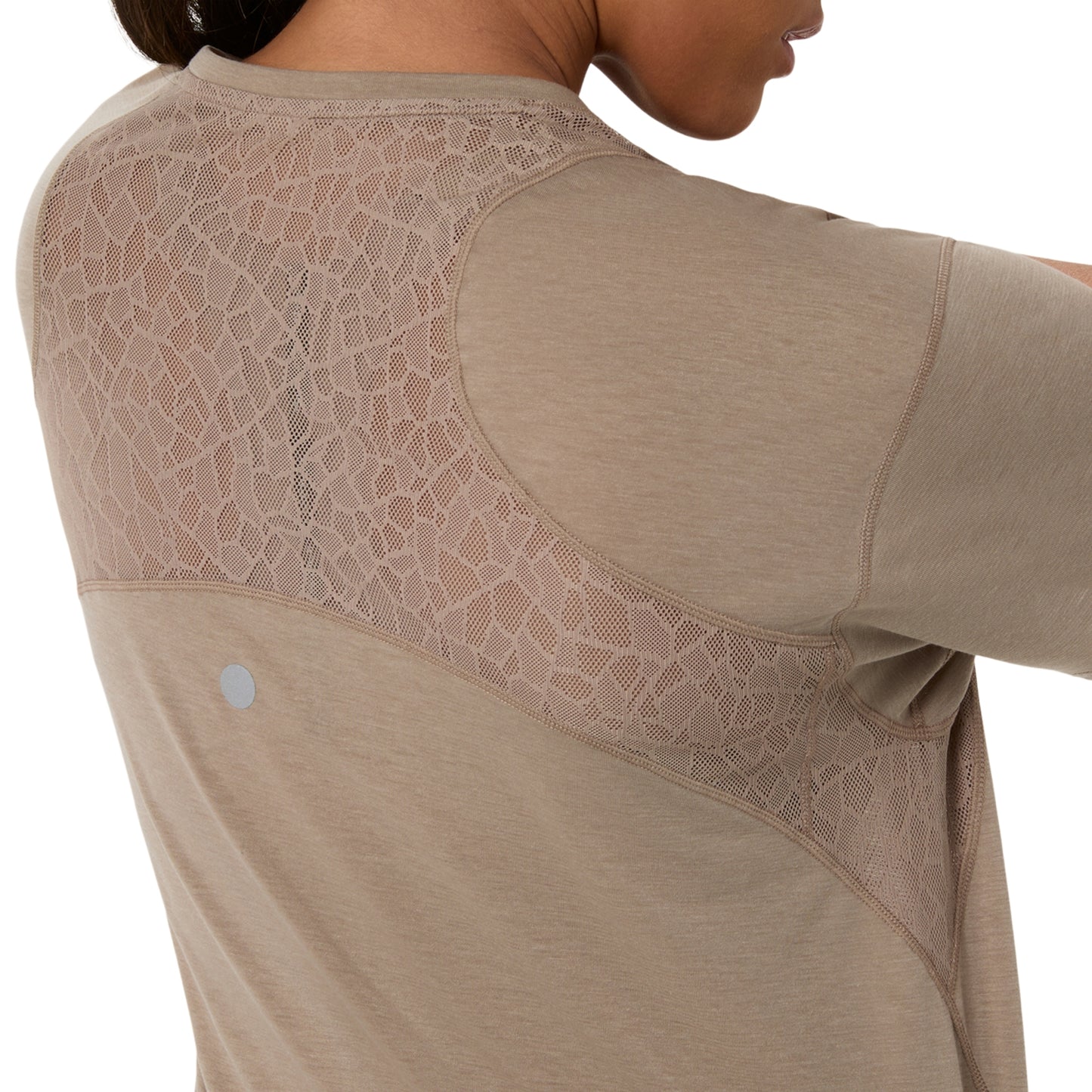 Close-up of a model wearing a beige athletic long-sleeve top, showing the back with a large textured mesh panel across the upper back and shoulders.