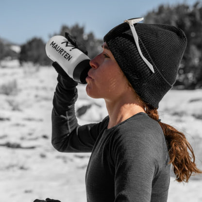 Person drinking from a Maarten water bottle in a snowy landscape