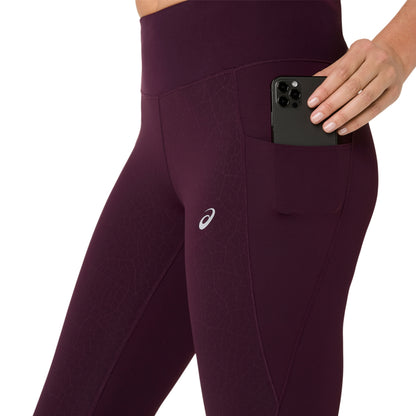 Close-up of a person wearing high-waisted athletic leggings in deep plum purple, showing a side pocket holding a black smartphone. The ASICS logo is visible on the thigh.