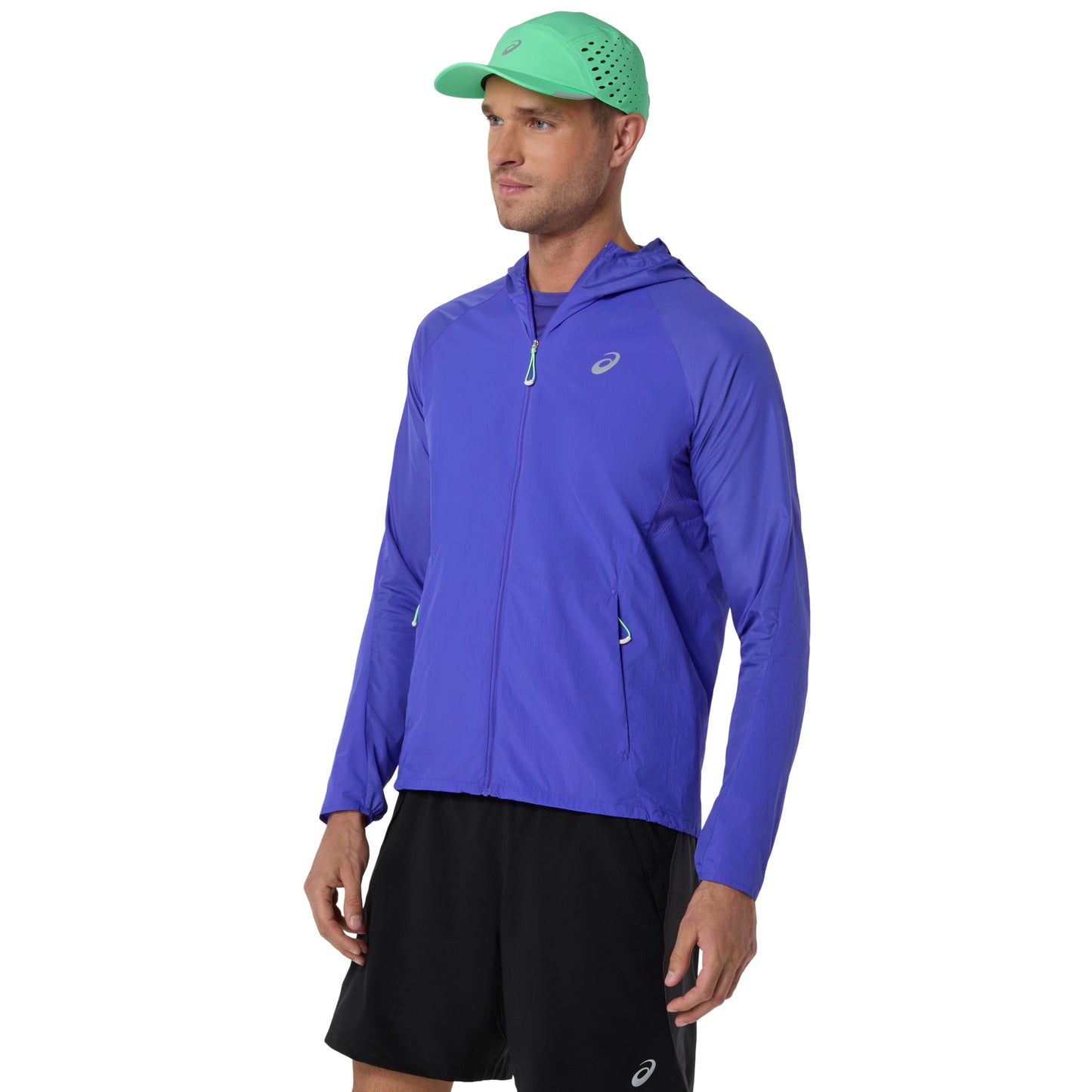 Man wearing a blue running jacket and black shorts with a green cap on a white background