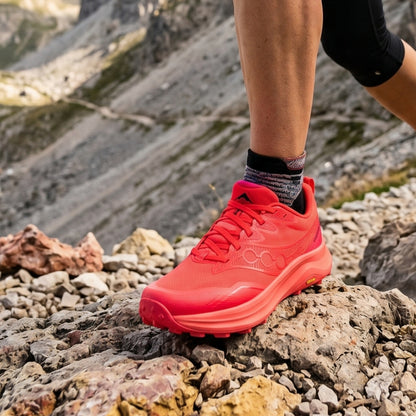 Person wearing a red Saucony running shoe on rocky terrain with mountains in the background