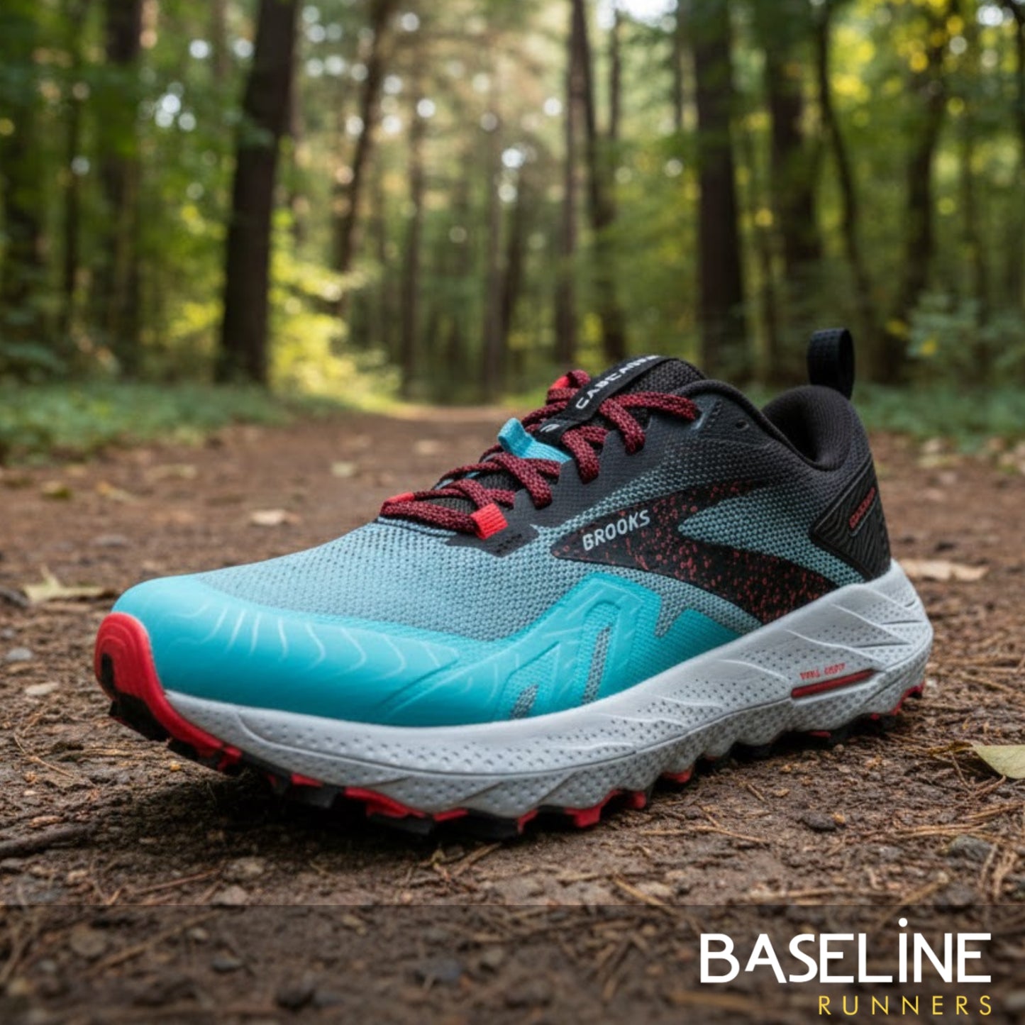 Blue and black running shoe with pink accents on a forest floor, featuring the Brooks brand.