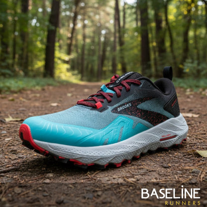 Blue and black running shoe with pink accents on a forest floor, featuring the Brooks brand.