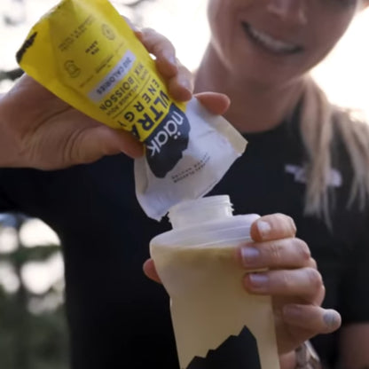Person pouring a supplement from a yellow and white package into a white cup.