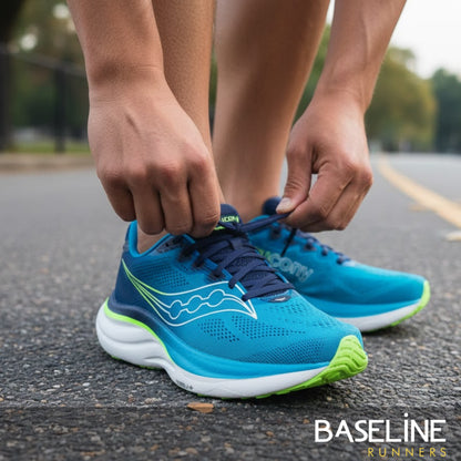 Person tying blue Saucony running shoes with green accents on a road.