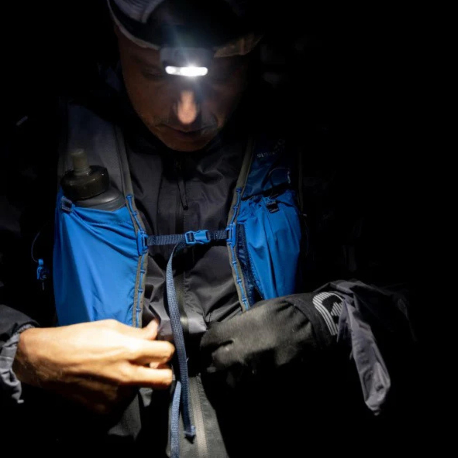 Person wearing a headlamp and blue hydration vest in the dark
