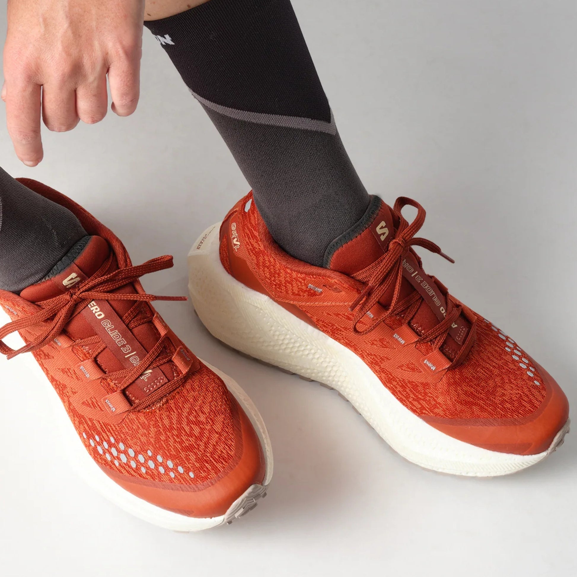 Person wearing red Salomon running shoes with white soles on a light gray background