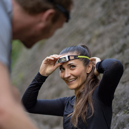 Woman adjusting a headlamp outdoors with a mountainous background