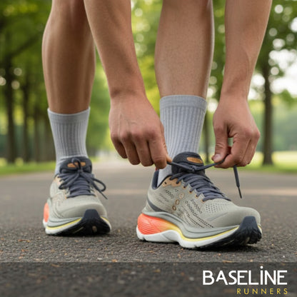 Person tying Saucony mens running shoes with 'Baseline Runners' branding in a park setting