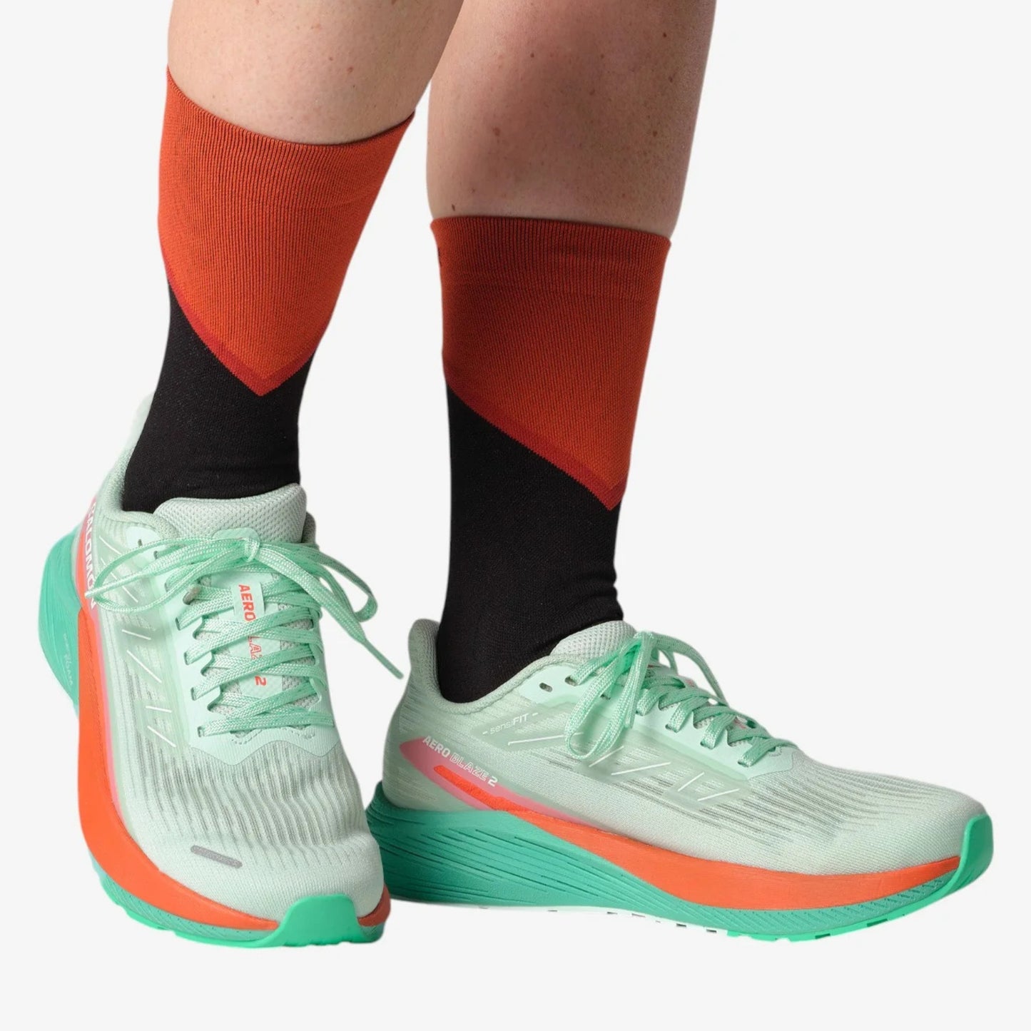 Light green running shoes with orange accents worn with red and black socks on a white background