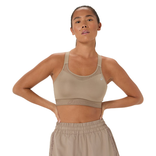 A woman modeling a beige Asics sports bra and matching athletic bottoms against a plain white background.