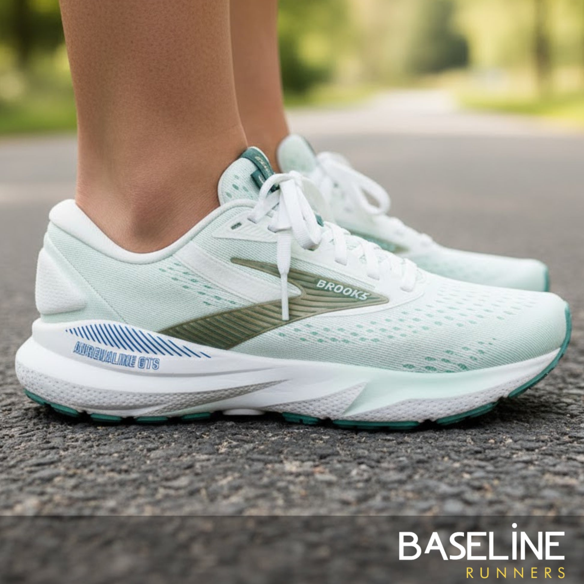 White running shoes with green and blue accents with white soles on a road, featuring the Brooks brand.