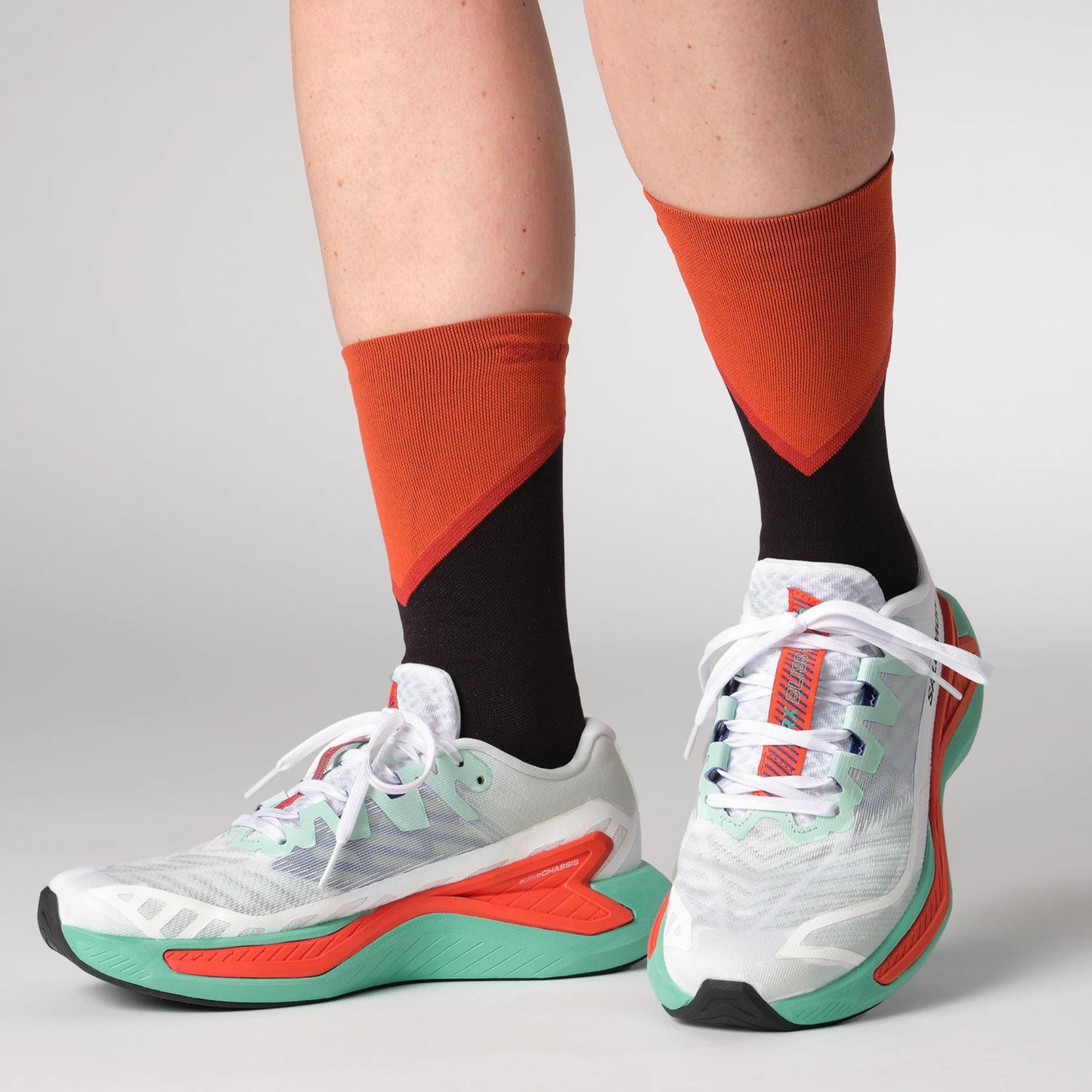 White Salomon running shoes with red and green accents worn with orange and black socks on a gray background