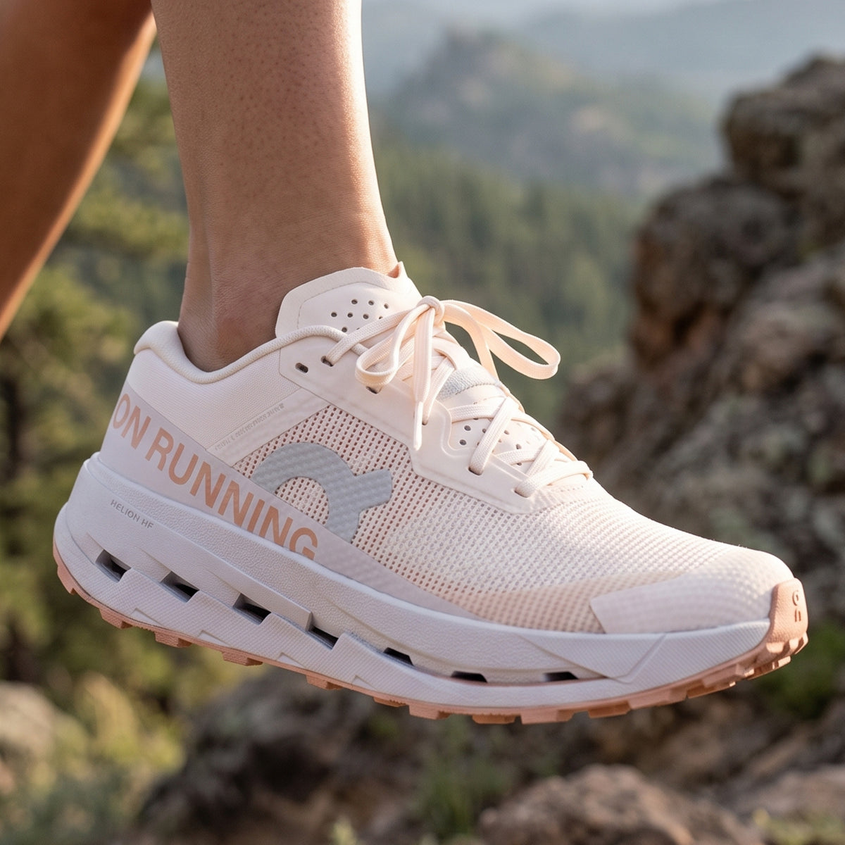 A close-up of a person's foot wearing a white and peach running shoe, set against a blurred mountain background.