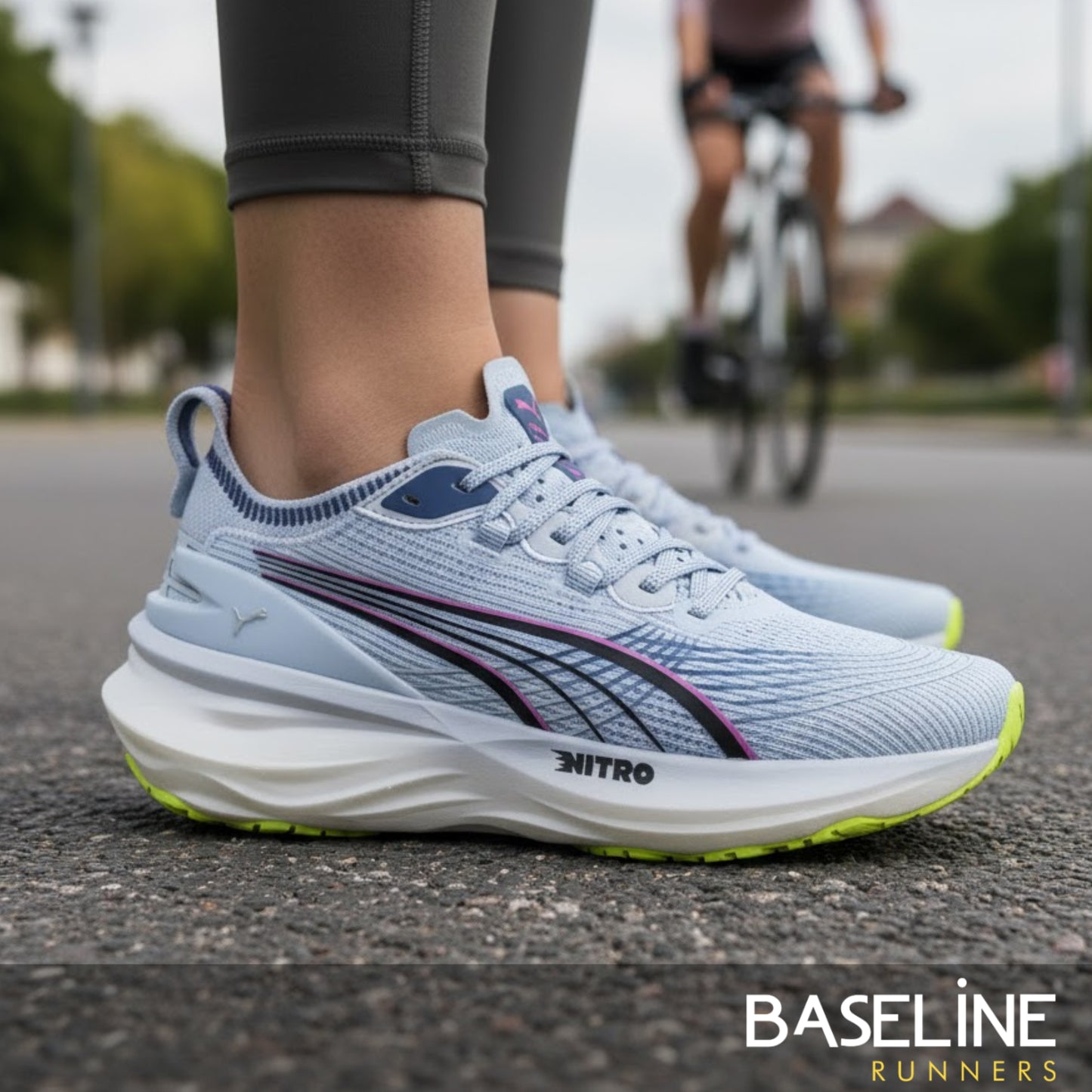Light blue Puma running shoes with green sole on a road, person cycling in the background