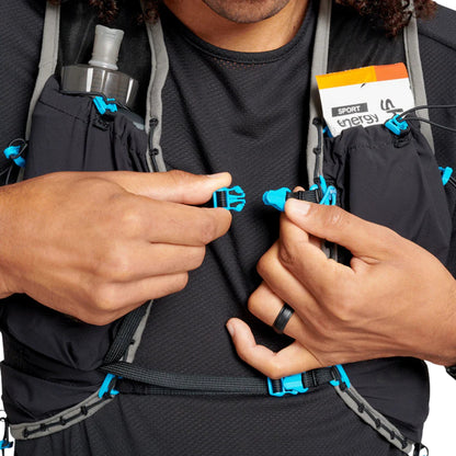 Person adjusting a black hydration pack with blue straps on a white background