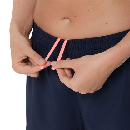 Person adjusting navy blue Asics shorts with pink waistband on a white background