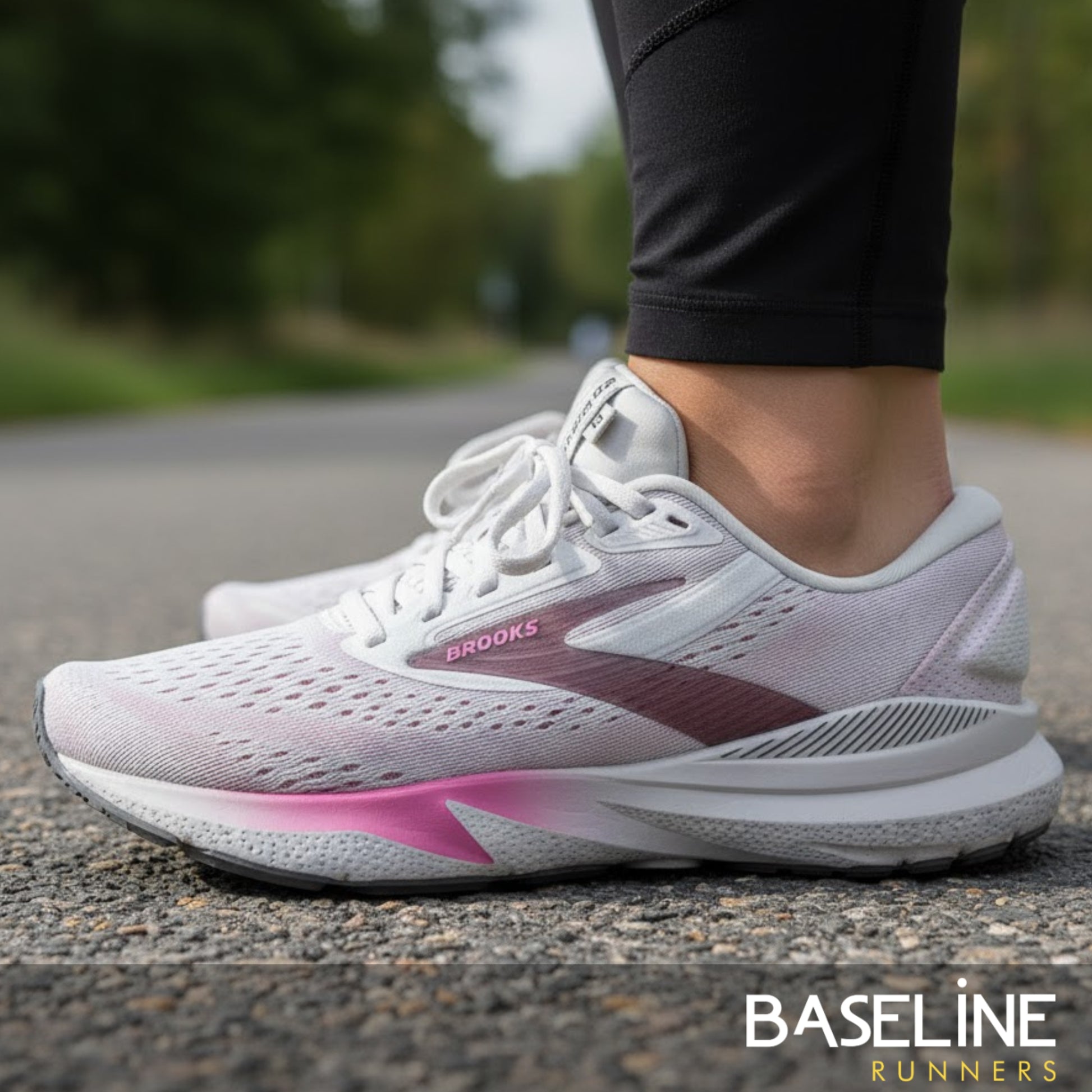 White and pink running shoes with 'Brooks' branding on a blurred outdoor background.