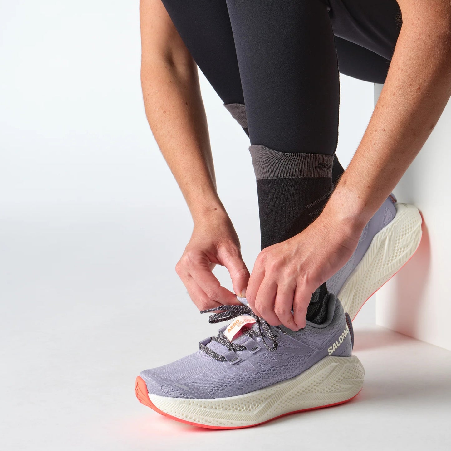 Person tying a purple Salomon running shoe with a white sole on a light background