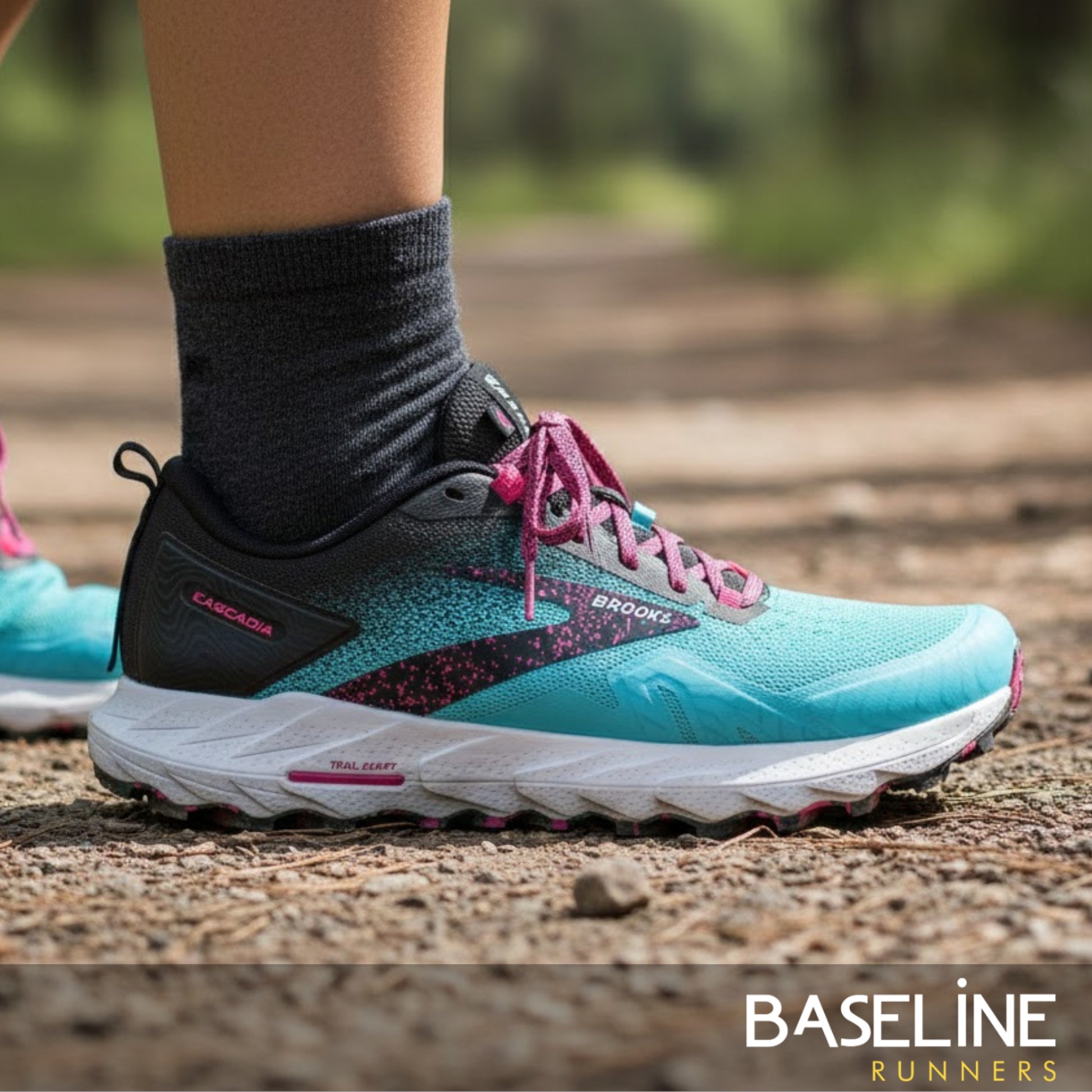 Blue and black running shoe with pink laces on a blurred natural background, featuring the Brooks brand.