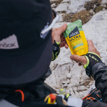 Person holding a naak Ultra Energy supplement packet in a mountainous area