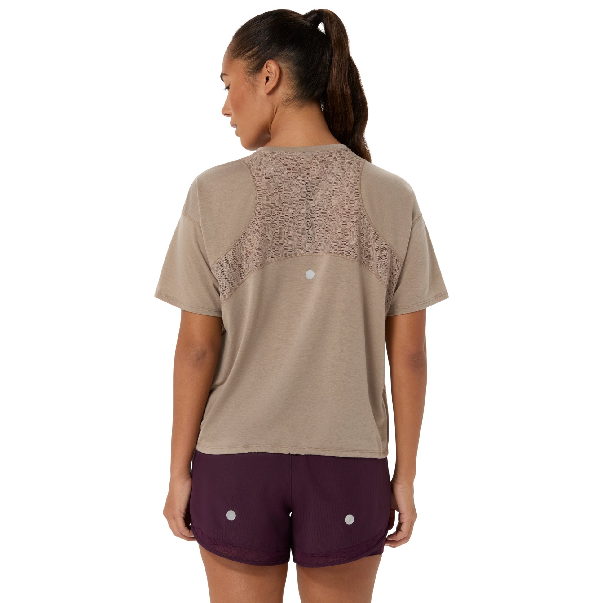 A woman shown from the back wearing a beige short-sleeve athletic top with a sheer lace panel across the upper back and dark plum athletic shorts, against a plain white background.