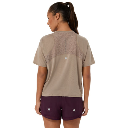 A woman shown from the back wearing a beige short-sleeve athletic top with a sheer lace panel across the upper back and dark plum athletic shorts, against a plain white background.
