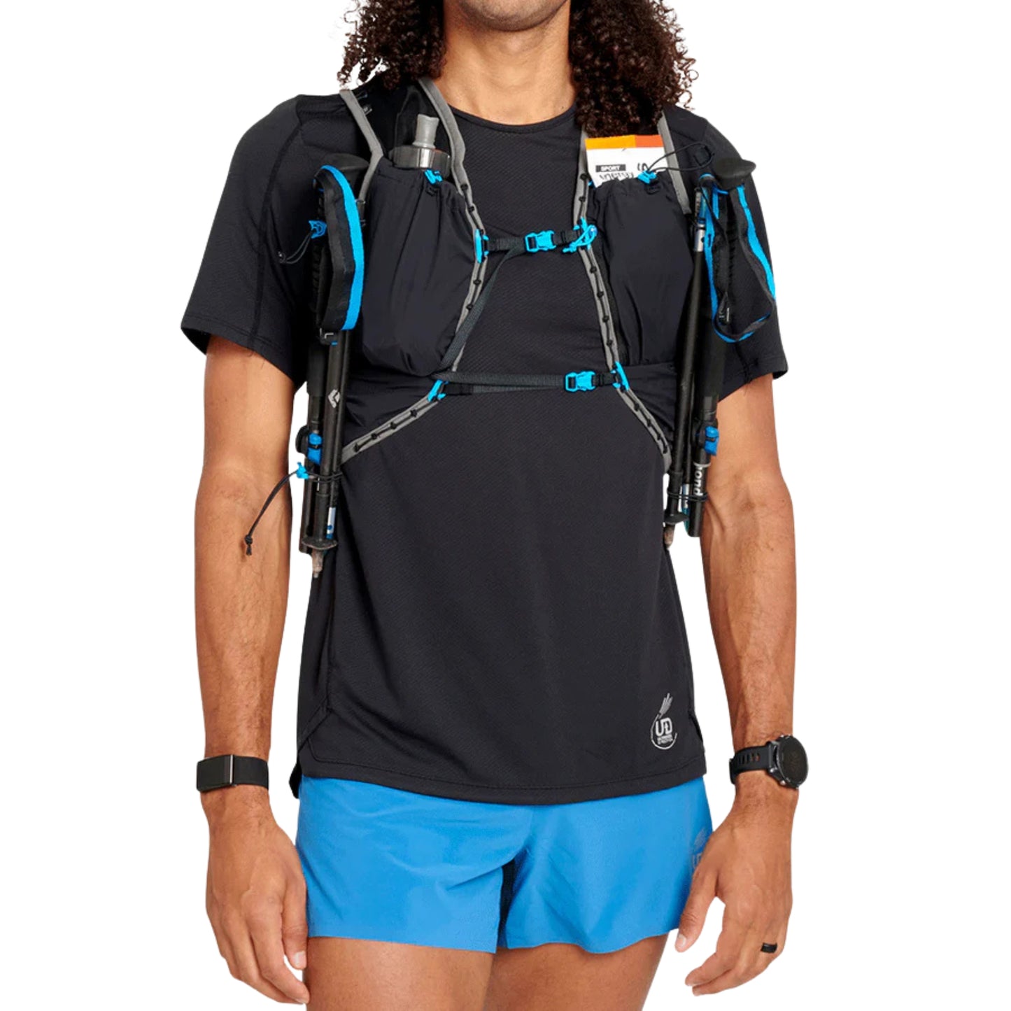 Person wearing a black t-shirt, blue shorts, and a black backpack with blue hydration vest on a white background