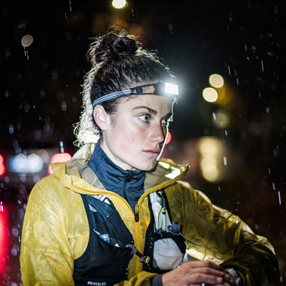 Person wearing a yellow jacket and headlamp in a snowy night setting