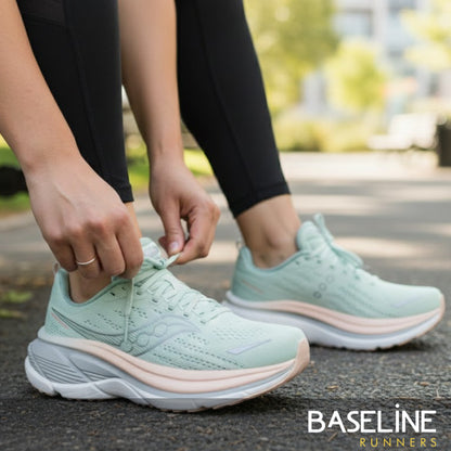 Person tying light green Saucony running shoes on a blurred outdoor background with 'Baseline Runners' branding.