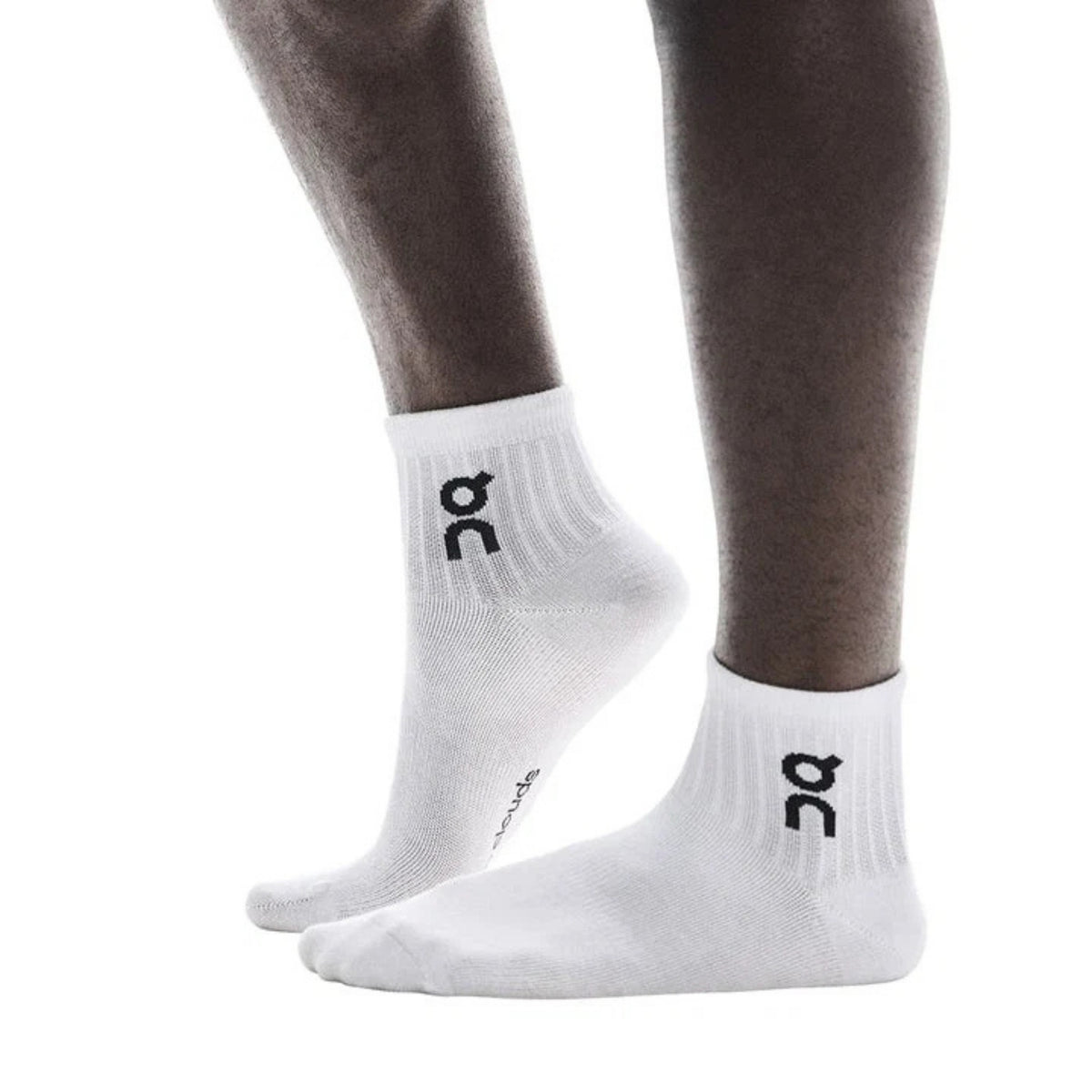 White low-cut athletic socks with a black logo on the ankle, shown on a person's feet against a plain white background.
