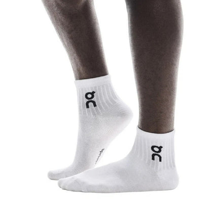 White low-cut athletic socks with a black logo on the ankle, shown on a person's feet against a plain white background.