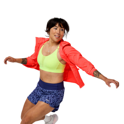 Woman wearing a orange jacket with a Brooks logo on a white background