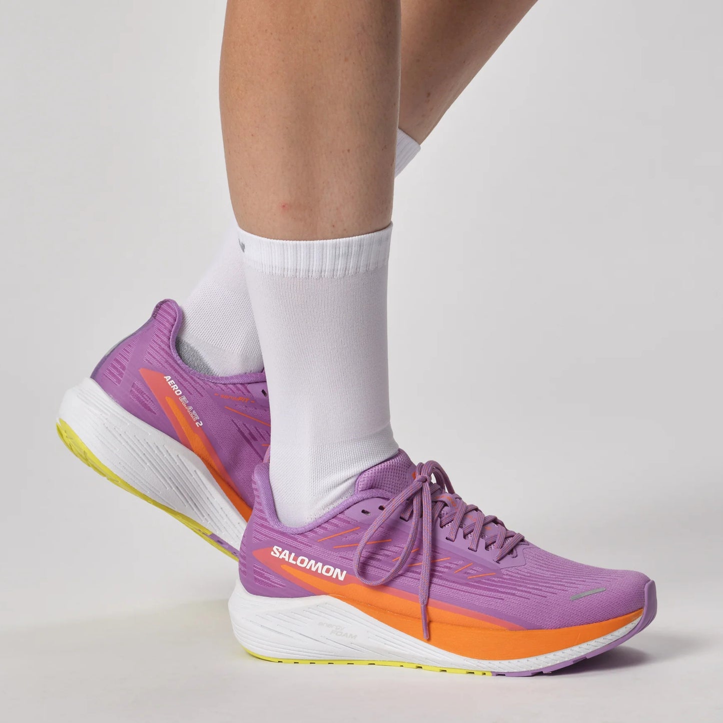 Purple Salomon running shoes with orange accents worn by a person on a light gray background