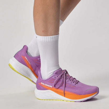 Purple Salomon running shoes with orange accents worn by a person on a light gray background
