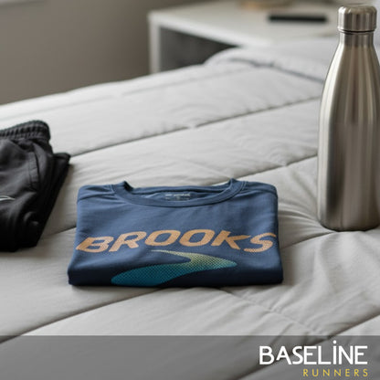 Folded blue shirt with 'Brooks' logo on a bed next to a water bottle, with 'Baseline Runners' branding.