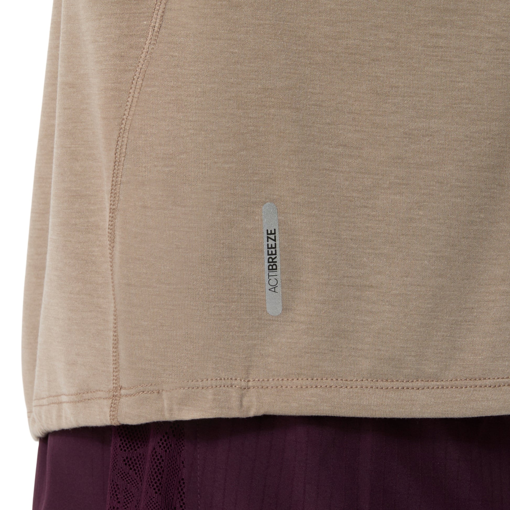 Close-up of a beige athletic top with a small vertical reflective strip reading ACTIBREEZE, shown against a white background with a dark purple garment partially visible below.