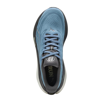 A top-down view of a Puma running shoe in light blue, gray, and black, featuring a breathable mesh upper, blue laces, and a cushioned sole.