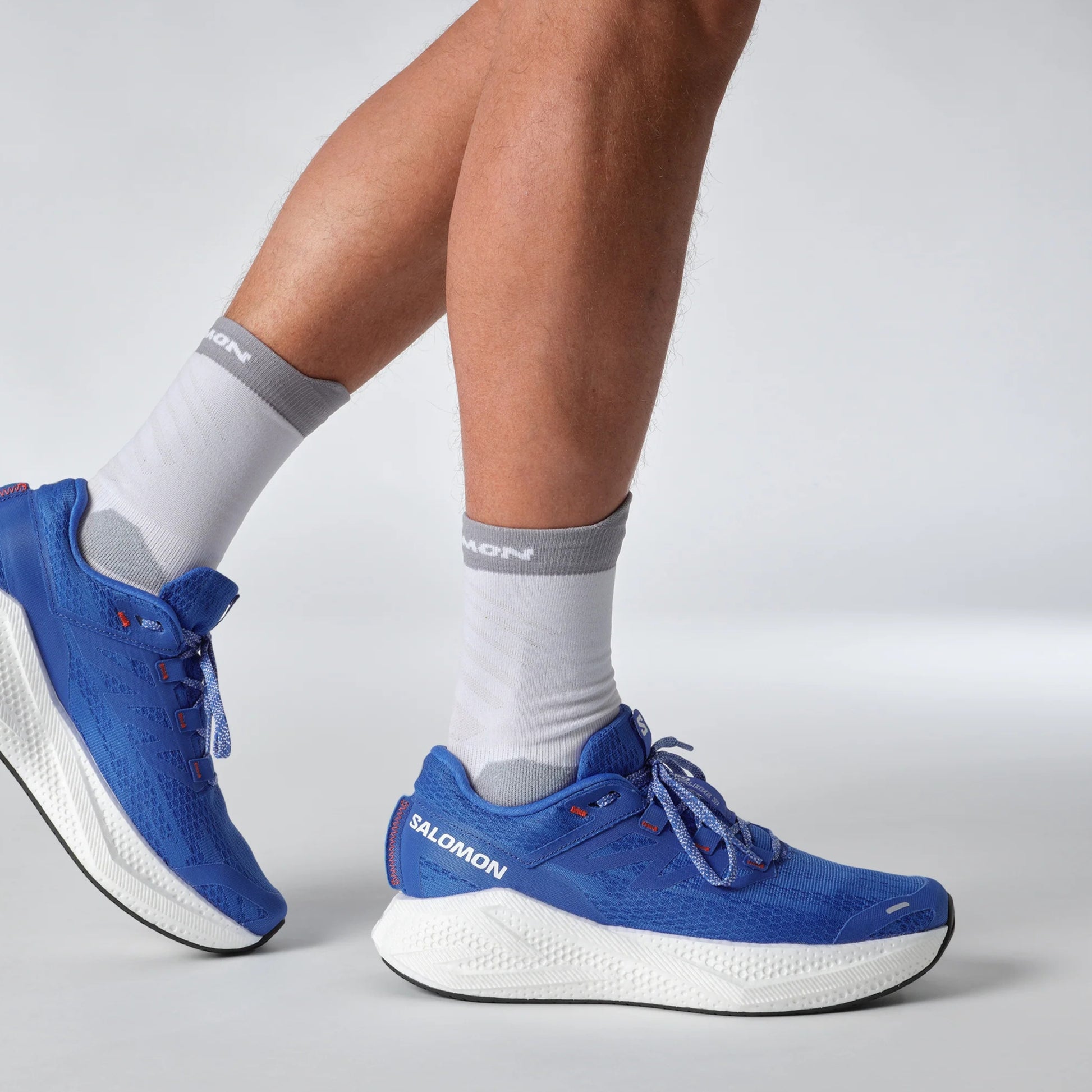 Blue Salomon running shoes with white soles worn by a person on a light gray background