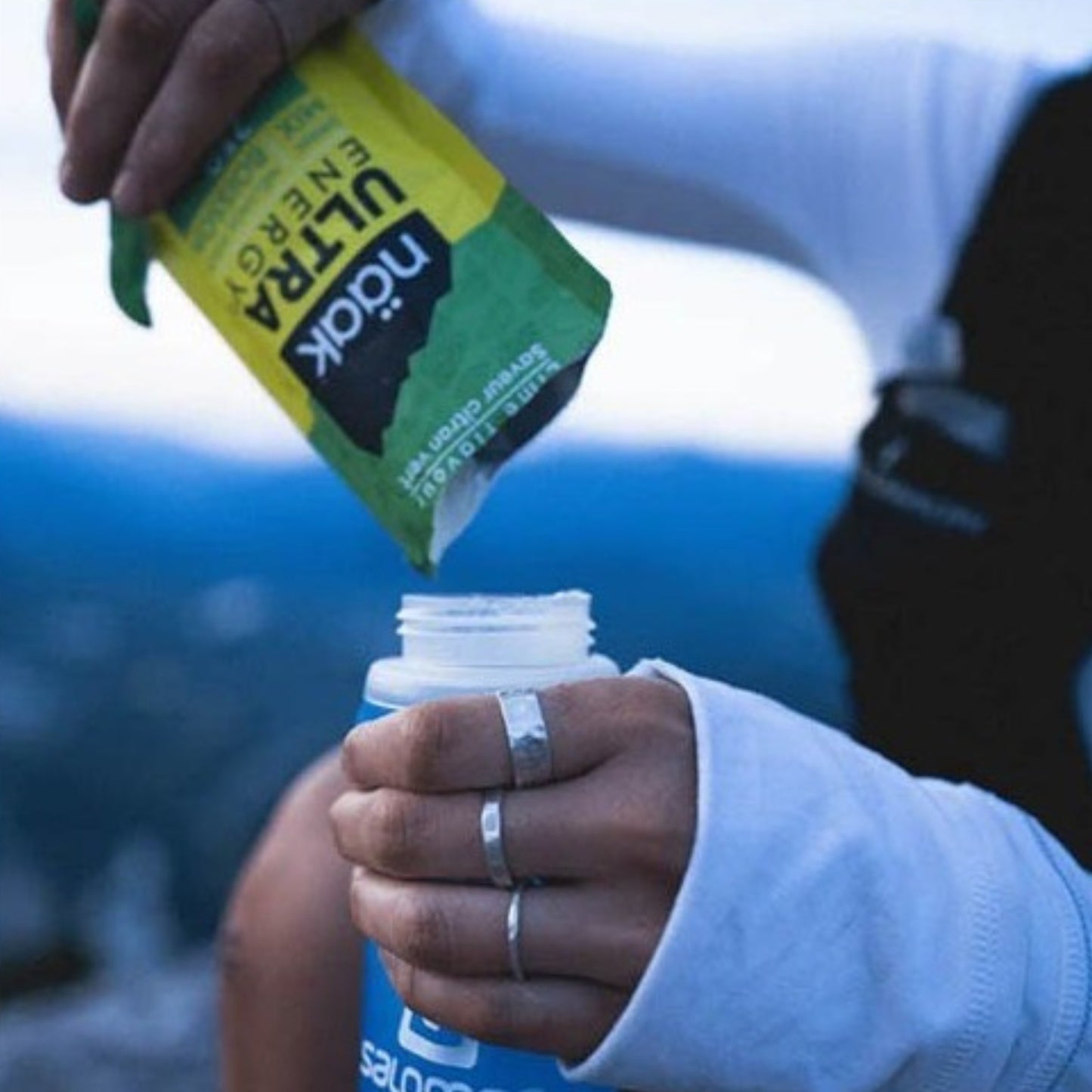 Person pouring Ultra Naak from a green packet into a bottle with a blurred background